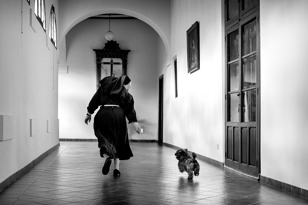 A nun and a dog in a convent corridor.